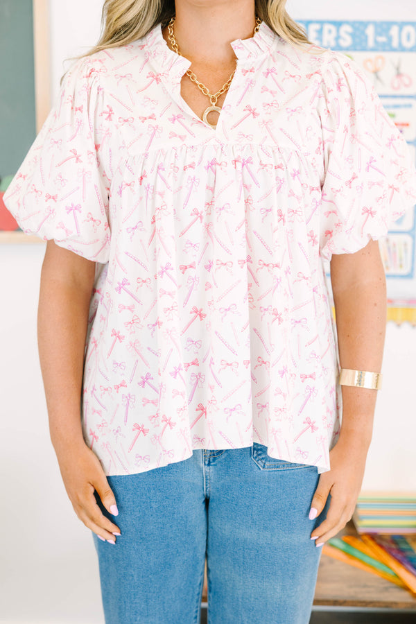 Plus Size pink and white blouse with pencil and bow print, ruffled v-neck, and bubble sleeves.