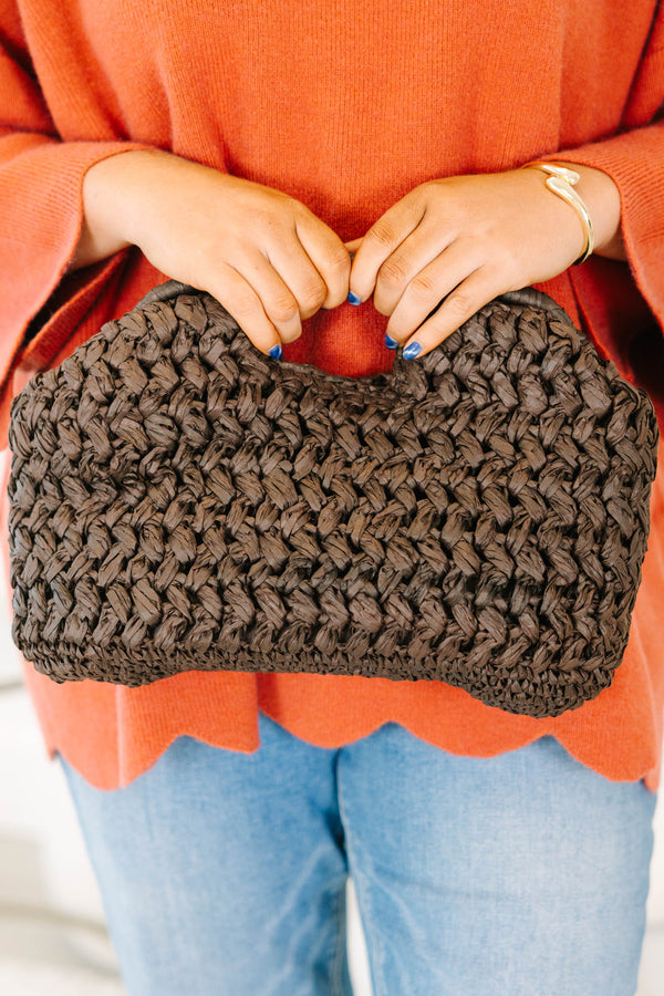 Plus Size brown woven straw clutch bag held with an orange knit sweater and blue jeans.