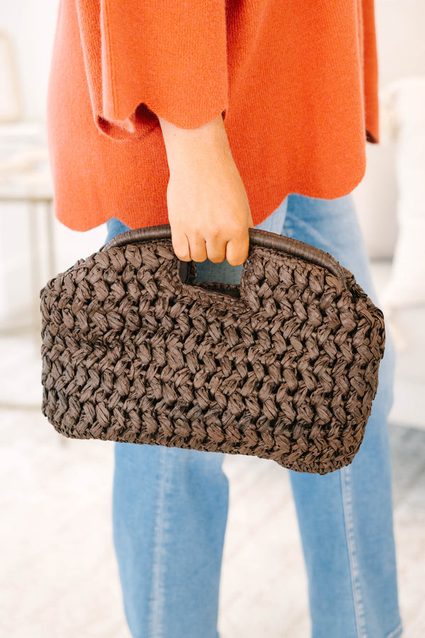 Plus Size brown woven straw clutch bag held with an orange knit sweater and blue jeans.