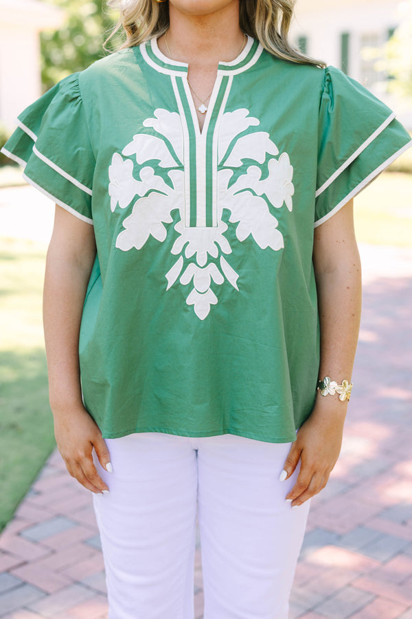Plus size sage green top with white floral appliqué, ruffle sleeves, and a flowy silhouette.