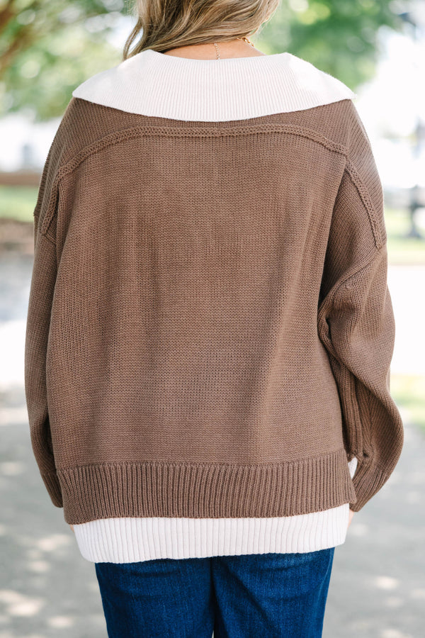 Plus size brown V-neck Sweater with a flowy fit and ribbed hem over blue jeans.