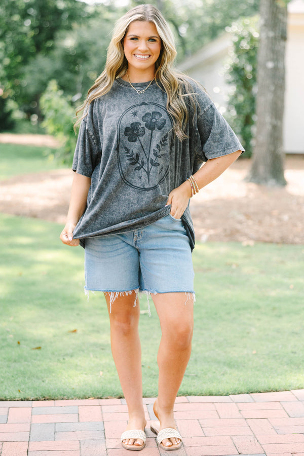 Plus size woman in a black acid wash relaxed tee with a floral graphic and light wash denim shorts.