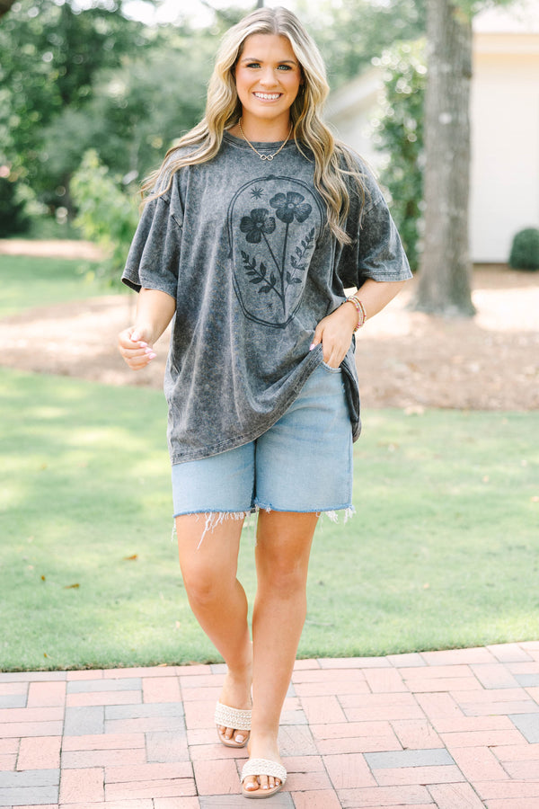 Plus size woman in a black acid wash relaxed tee with a floral graphic and light wash denim shorts.
