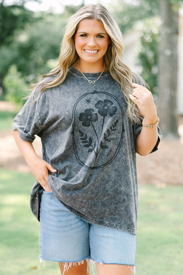 Plus size woman in a black acid wash relaxed tee with a floral graphic and light wash denim shorts.