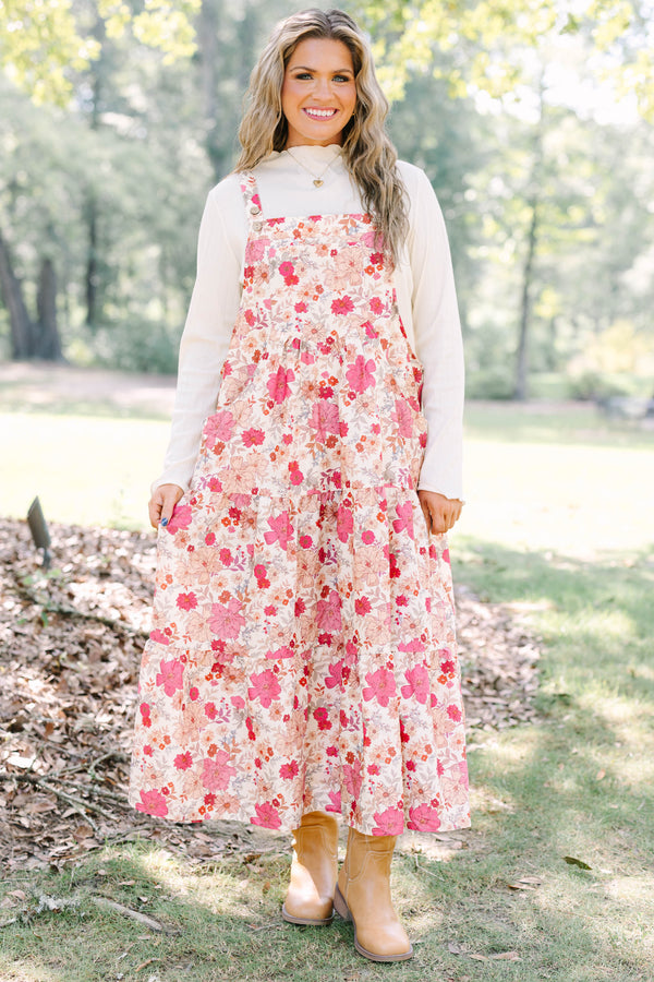 Plus Size pink floral tiered midi dress with overall straps over a white long-sleeve top.