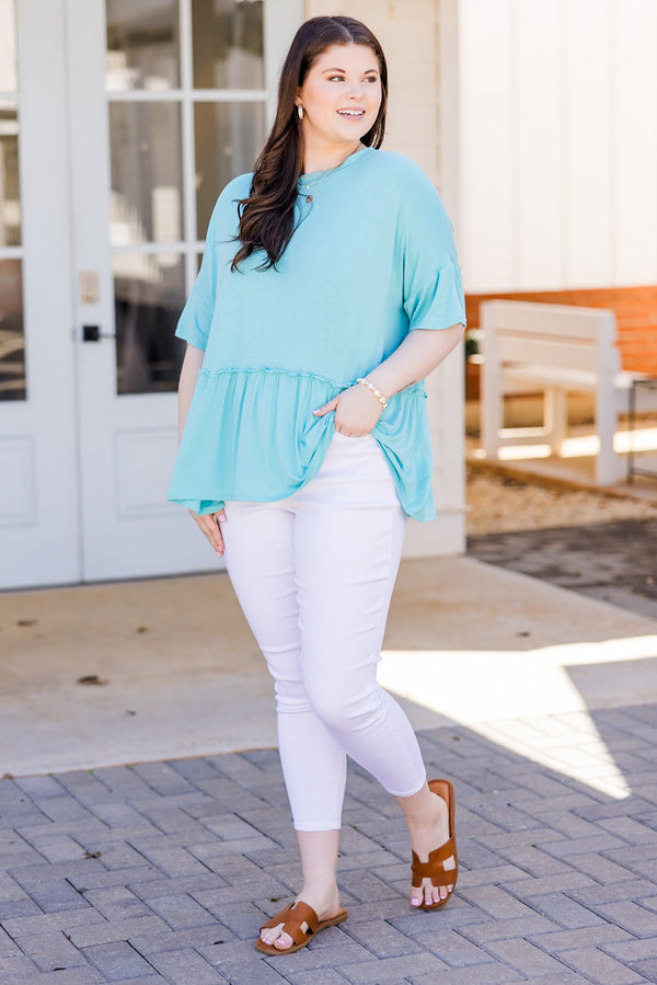 Plus Size seafoam short-sleeve top with a ruffle hem and crew neckline paired with white pants.