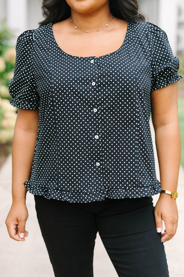 Short-sleeve black and white polka-dot blouse featuring a scoop neckline, front button closure, and a playful ruffled hem