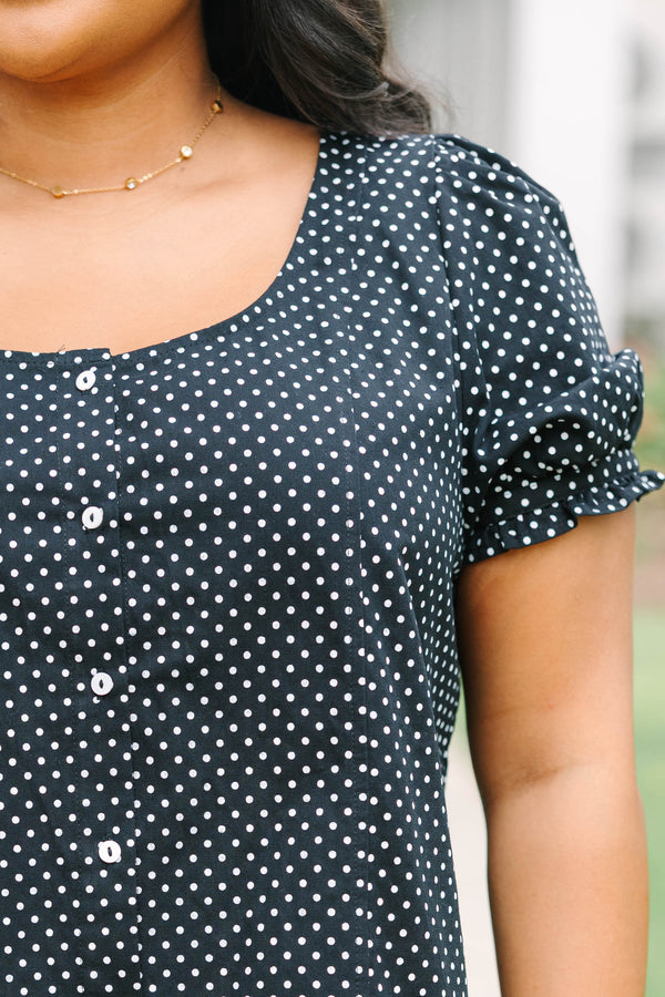 Short-sleeve black and white polka-dot blouse featuring a scoop neckline, front button closure, and a playful ruffled hem