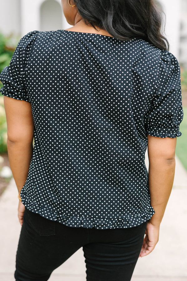 Short-sleeve black and white polka-dot blouse featuring a scoop neckline, front button closure, and a playful ruffled hem