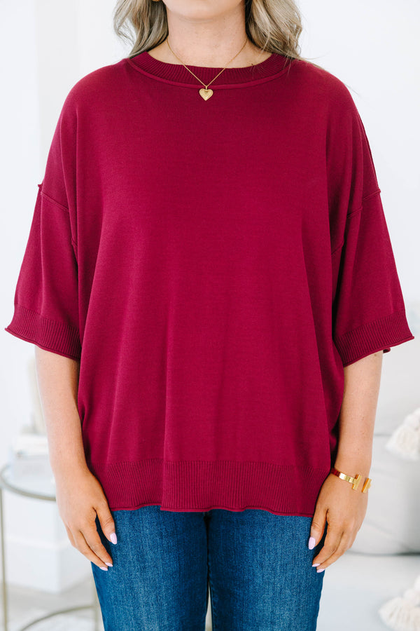 Plus size woman in a garnet red, oversized knit sweater with a flowy fit and short dolman sleeves.