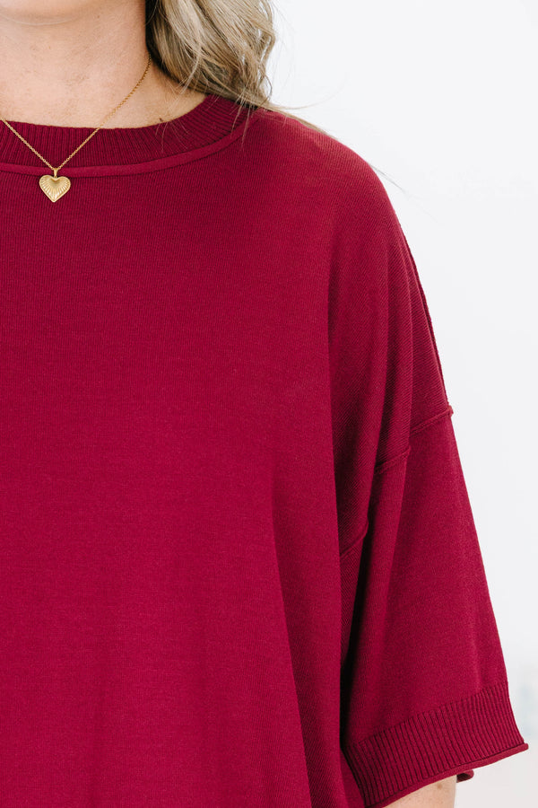 Plus size woman in a garnet red, oversized knit sweater with a flowy fit and short dolman sleeves.