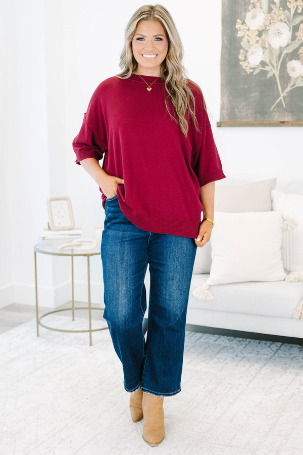 Plus size woman in a garnet red, oversized knit sweater with a flowy fit and short dolman sleeves.