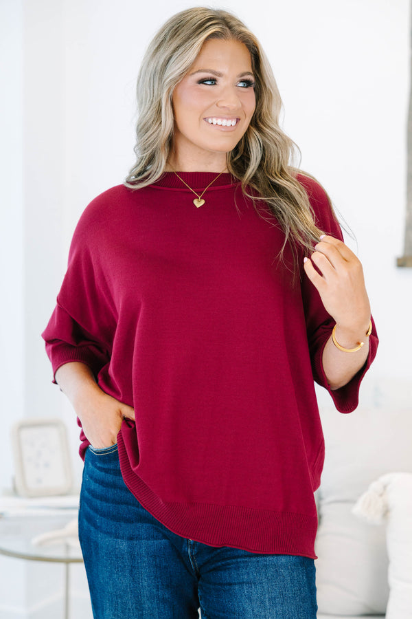 Plus size woman in a garnet red, oversized knit sweater with a flowy fit and short dolman sleeves.