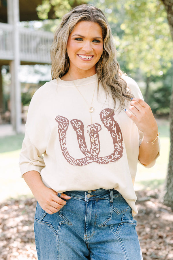 Plus Size cream short sleeve sweater with a brown horseshoe graphic and blue denim jeans.