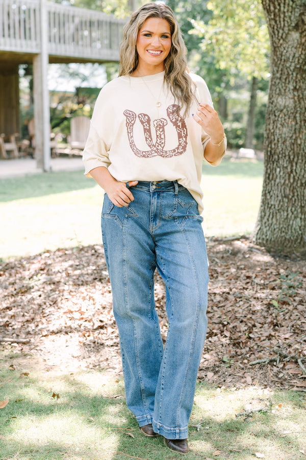 Plus Size cream short sleeve sweater with a brown horseshoe graphic and blue denim jeans.