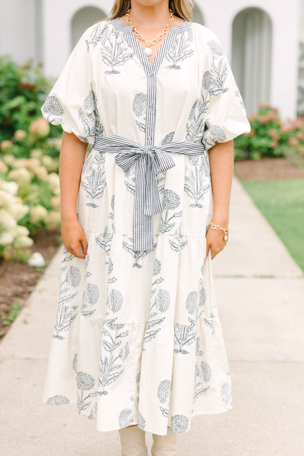 Plus size cream tiered midi dress with navy blue floral print, blue striped sash, and puff sleeves.