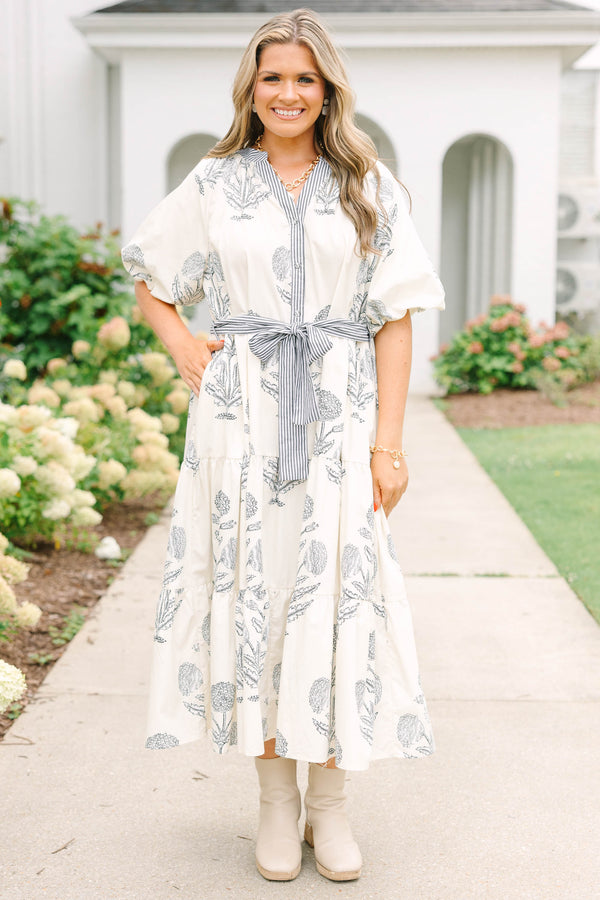Plus size cream tiered midi dress with navy blue floral print, blue striped sash, and puff sleeves.