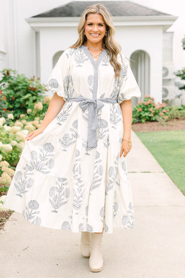Plus size cream tiered midi dress with navy blue floral print, blue striped sash, and puff sleeves.