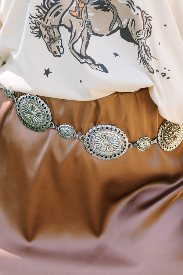 Plus Size silver concho chain belt with intricate sunburst engravings over a brown satin skirt.