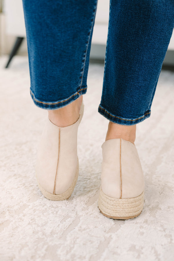A person wearing sand-colored platform wedge mules with a woven jute sole