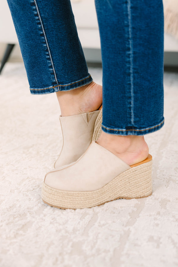 A person wearing sand-colored platform wedge mules with a woven jute sole