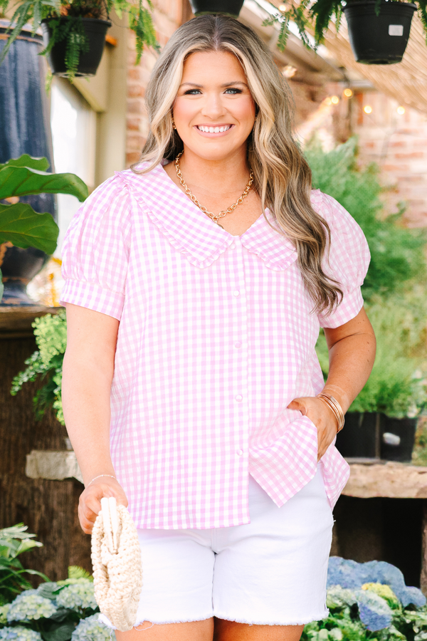 Chic Soul plus size clothing, pink button up top with short sleeves that have cuffs at the end of the sleeves as well as a bib detail on the shoulders that has ruffle detailing and a pink gingham pattern throughout 
