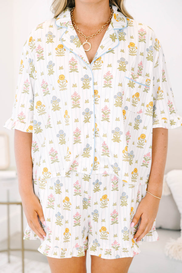 Plus Size white floral pajama set with short sleeves, button-down top, and matching ruffled shorts.