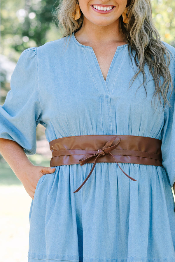 Plus Size brown faux leather wrap belt tied in a bow over a light blue denim dress.