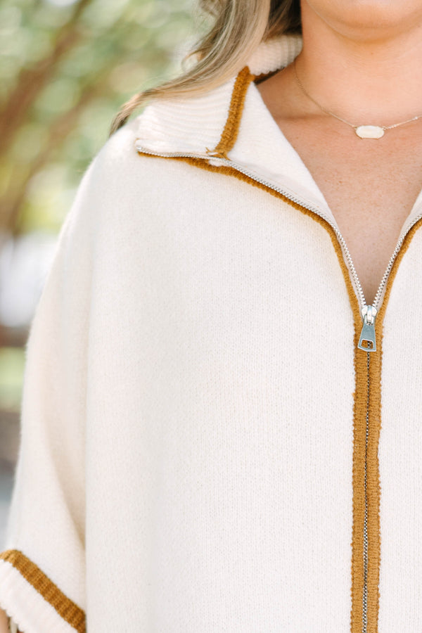 Plus size cream zip-up poncho sweater with brown trim, front pockets, and a flowy, relaxed fit.