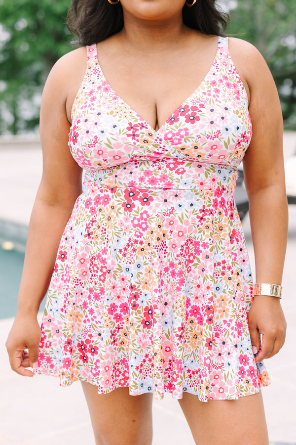 A woman smiles in a pink floral swim dress with a V-neckline and flared skirt.