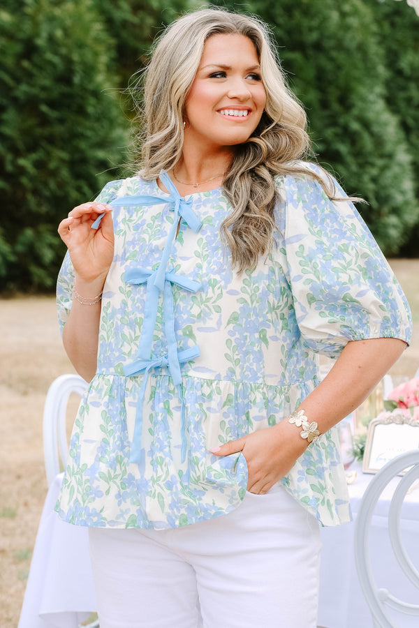 Chic Soul plus size clothing, white puff short sleeve babydoll top with light blue and green floral pattern and three blue bow ties down the middle of the top and cinching at the end of the sleeves