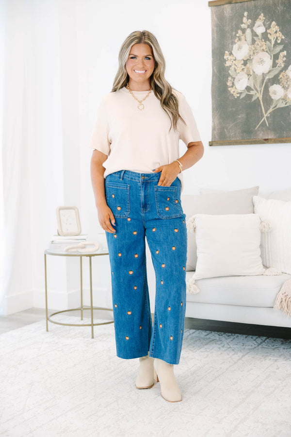 Plus size wide leg blue denim jeans with all-over pumpkin embroidery and a raw hem.