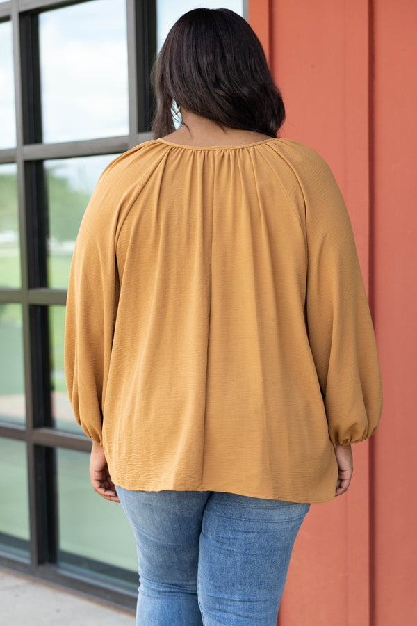 Plus Size toffee-colored v-neck top with bubble sleeves and distressed blue denim jeans.